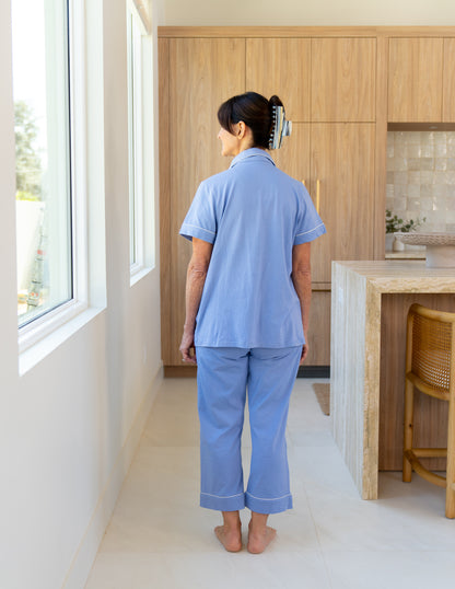 Woman wearing a blue recovery pajama set standing in a modern kitchen, showing the length of the pants. They are just above the ankle, model is 5'5