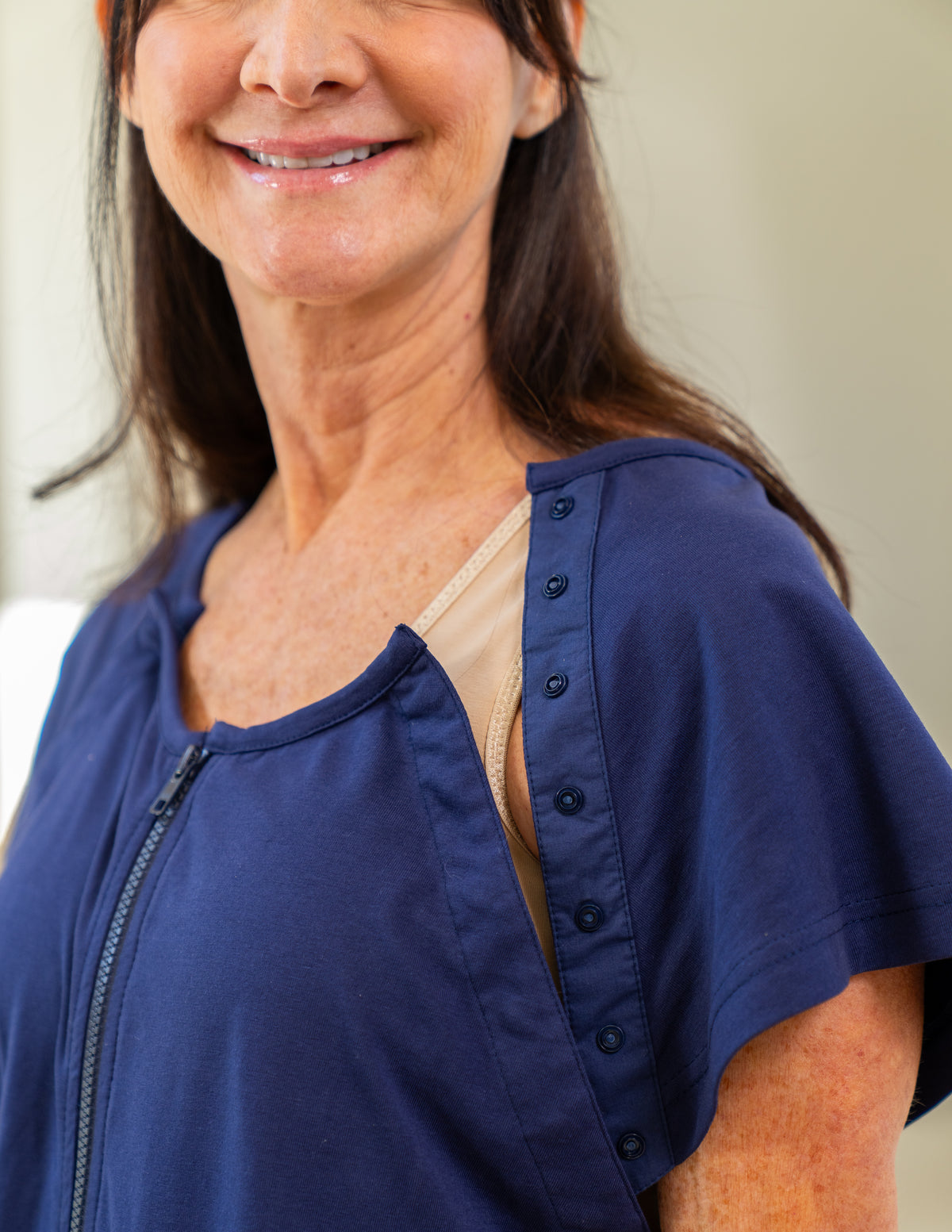 Woman wearing a blue hospital gown with a snap opening on the chest for port access.