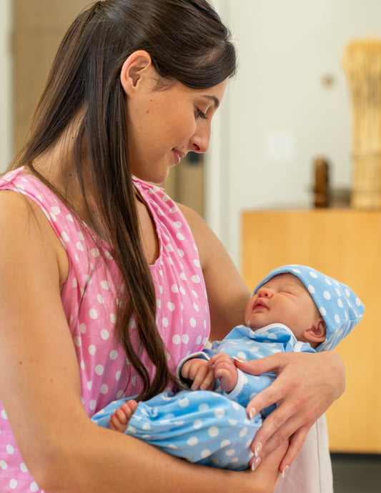 Woman in pink hospital gown holding a baby wrapped in a blue and white polka dot set indoors.