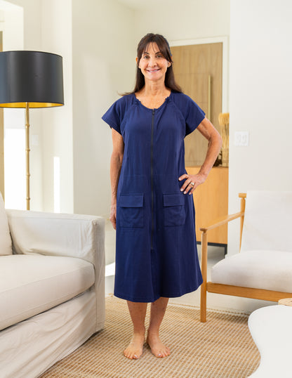 Woman wearing a blue recovery gown with drain management pockets hidden inside standing in a living room.