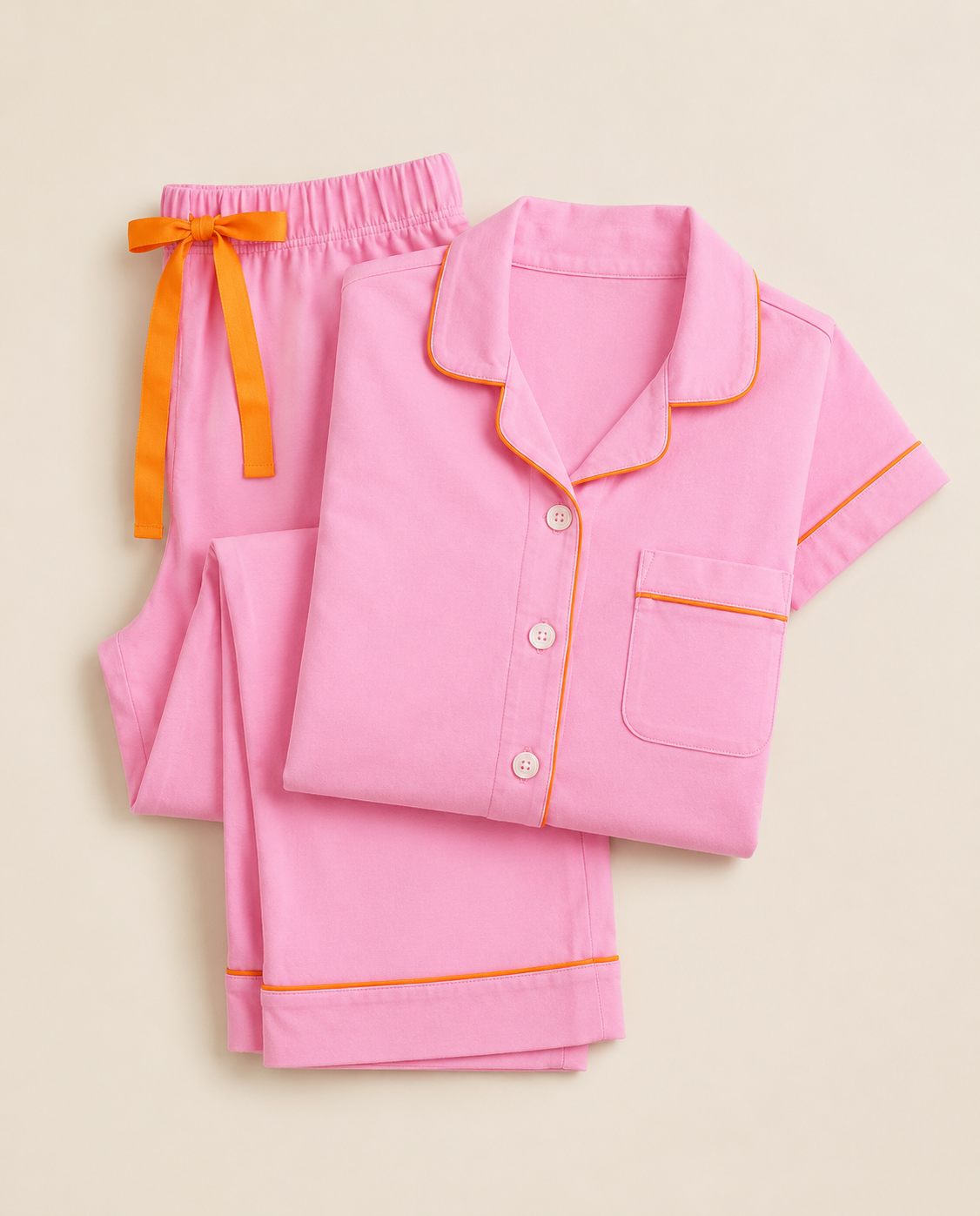 A pink short-sleeve pajama set with orange piping and a matching orange drawstring tie, shown on a light beige background.