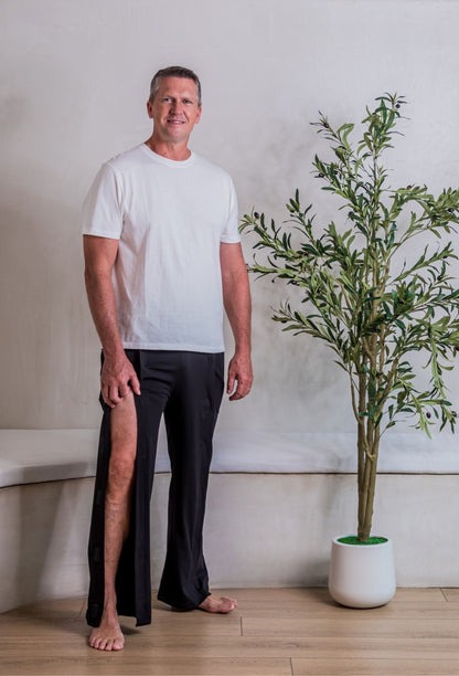 A man wearing a white crewneck t-shirt and black tearaway pants, open up high to show leg accessibility for things like physical therapy, suture or stitch removal, braces and immobilizers, and leg IV access.